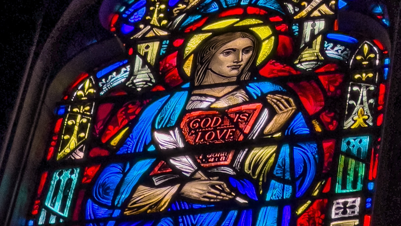Detail of a stained glass window in St. John's Episcopal Church, Youngstown, Ohio depicting John holding a quill and scripture showing the words "God is love" (John 4:8).